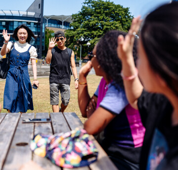 Students sitting on a bench greeting their friends coming towards them