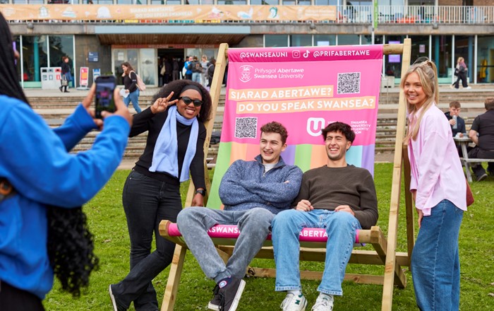 A small group of happy-looking students sit on a giant deckchair outside Fulton House 